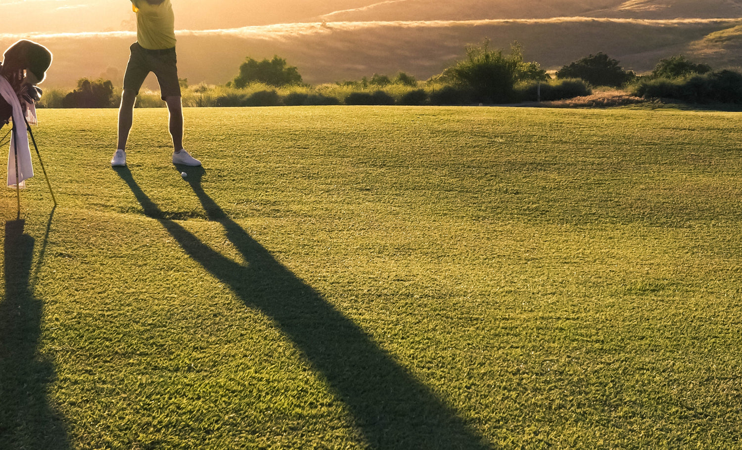 A golfer in silhouette swings his club on a serene golf course, with a breathtaking sunset painting the sky in vibrant hues in the background.